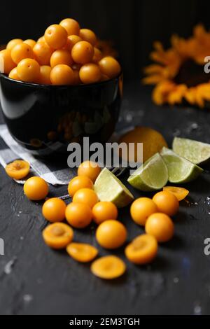 Prunes jaunes avec citron et lime sur fond noir. Ingrédients pour une confiture-prunes savoureuses. Photographie alimentaire. Image verticale. Tournesol jaune Banque D'Images