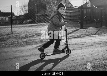 garçon de 5 ans à bord d'un scooter. Paysage de village. Banque D'Images