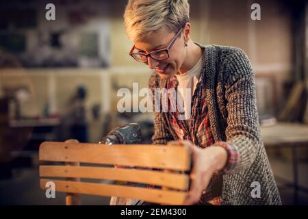 Vue rapprochée de la femme d'âge moyen, blonde et cheveux courts, assise sur la chaise dans l'atelier et posant tout en regardant loin. Banque D'Images