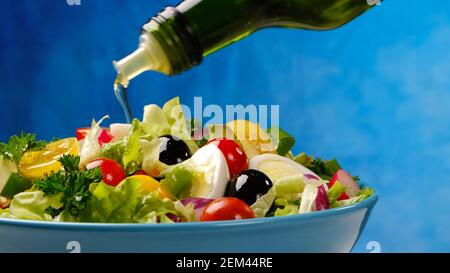 Huile d'olive déversé de la bouteille sur une salade de légumes frais Banque D'Images