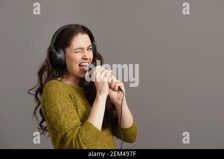 une adolescente chante avec un micro et un casque, isolée sur le gris Banque D'Images