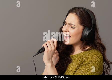 une adolescente chante avec un micro et un casque, isolée sur le gris Banque D'Images