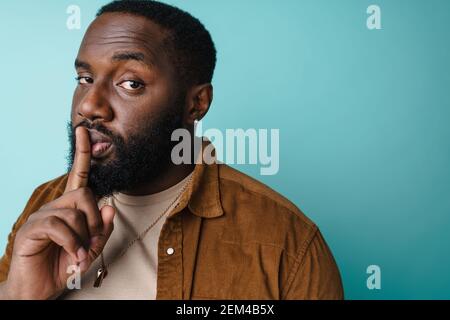 Heureux afro-américain homme montrant le geste de silence à la caméra isolée sur fond bleu Banque D'Images