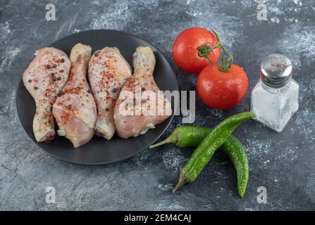 Pilon de poulet cru épicé à la tomate, au sel et au poivre sur fond gris Banque D'Images