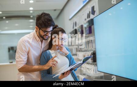 Vue rapprochée de l'attrayant happy excited hipster jeune amour couple debout près du grand téléviseur smart tv alors qu'une fille tient la spécification dans Banque D'Images