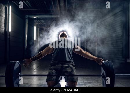 Vue portrait d'un homme bodybuilder à cheveux courts et musclés accroupir avec les mains ouvertes avant l'entraînement de force avec un poids lourd haltère Banque D'Images