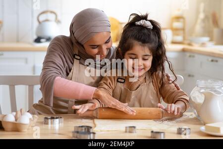 Maman musulmane montrant à sa petite fille comment faire rouler la pâte Pour les cookies Banque D'Images