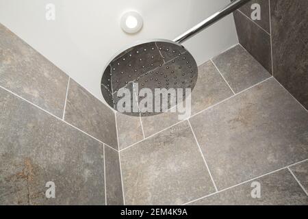 Une grande pomme de douche moderne dans une douche carrelée de gris Banque D'Images