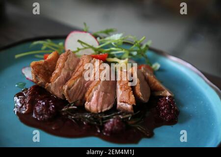 Confit de canard avec salade , pomme au four et sauce aux framboises servi sur table en bois Banque D'Images
