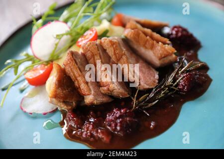 Confit de canard avec salade , pomme au four et sauce aux framboises servi sur table en bois Banque D'Images