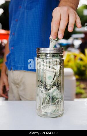 Vue en coupe d'un homme qui pose une facture d'un dollar dans un bocal Banque D'Images