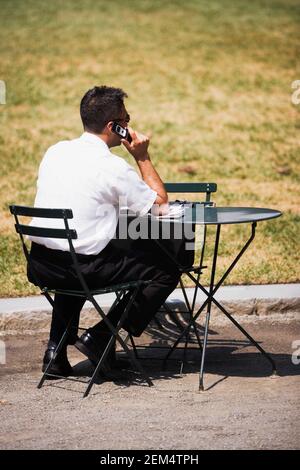Vue arrière d'un jeune homme assis sur une chaise et parler sur un téléphone portable Banque D'Images