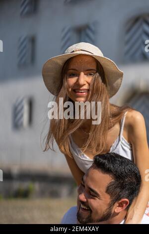 Jeune asiatique portant une belle jeune femme sur ses épaules. Le couple est souriant et riant au soleil avec la maison en arrière-plan. Banque D'Images