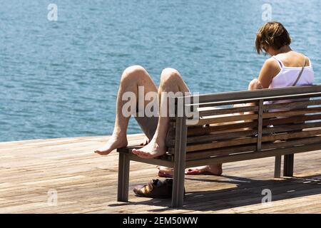 Vue arrière d'une femme assise sur un banc et d'un homme couché sur un banc, Barcelone, Espagne Banque D'Images