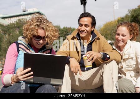 Deux jeunes femmes et un jeune homme assis ensemble et regarder un album photo Banque D'Images