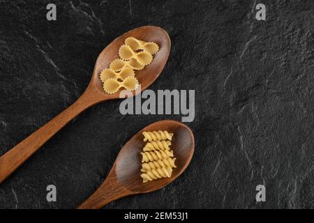 Cuillères en bois pleines de pâtes de girandole et de tonde farfalle crues Banque D'Images