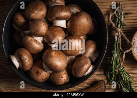 Bol de petits champignons bella et bouquet de romarin frais sur fond rustique en bois, vue d'en haut, nourriture à base de plantes, gros plan Banque D'Images