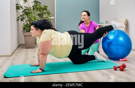 Entraîneur personnel de femme aidant la femme en surpoids faire des exercices de muscle de jambe. Entraînement, vue latérale Banque D'Images