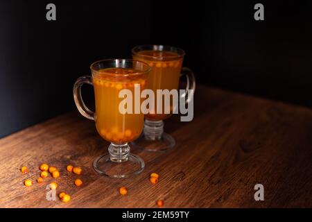 Boissons chaudes de l'argousier dans deux verres sur fond noir. Le concept des boissons chaudes de saison. Baies d'argousier à proximité. Boissons saines. H Banque D'Images