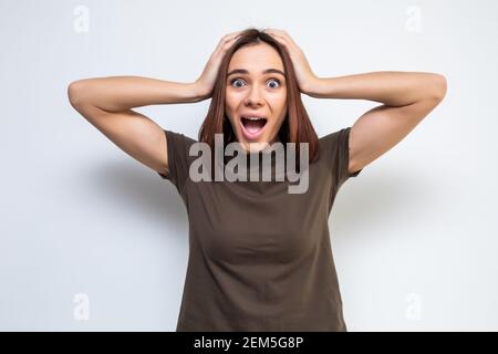 portrait de attrayant surpris excité peur hurlant adolescent, tenir les mains sur la tête, bouche ouverte avec les cheveux longs bruns, isolé sur fond blanc Banque D'Images