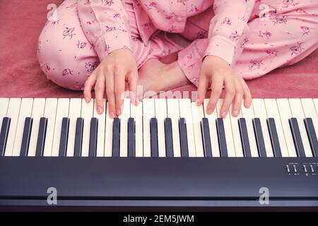 Femme en pyjama apprenant à jouer du piano assis dans le lit, les mains de près Banque D'Images