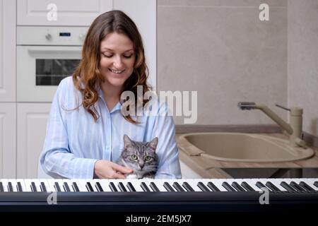 Une femme heureuse dans une nuit bleue et un drôle les animaux de compagnie apprennent à jouer du piano dans leur cuisine Banque D'Images