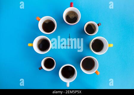 Heure du café. Composition avec café noir dans des tasses lumineuses et aiguilles d'horloge au centre de l'arrière-plan bleu. Vue de dessus. Copier l'espace. Banque D'Images