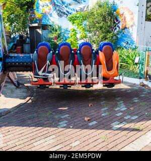 Attraction avec des sièges vides dans un parc d'attractions sur fond d'un buisson et d'un mur peint brillant Banque D'Images