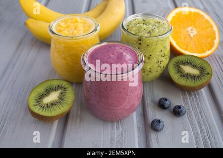 Différents smoothies de fruits ou purée dans les petits pots en verre sur fond de bois gris. Gros plan. Banque D'Images