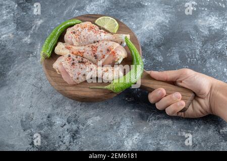 Pattes de poulet crues sur planche à découper en bois dans la main de l'homme Banque D'Images