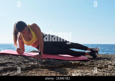 Femme latine, d'âge moyen, avec haut jaune, leggings noirs, entraînement, faire des exercices physiques, planche, abs, pas de grimpeur, calories brûlantes, maintien de f Banque D'Images