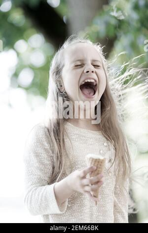 La crème glacée la fait tomber dans l'euphorie. Cute little girl eating ice cream on journée d'été. Petit enfant de lécher la crème glacée à l'extérieur du cône. Adorable happy kid appréciation des crème glacée dessert. Banque D'Images