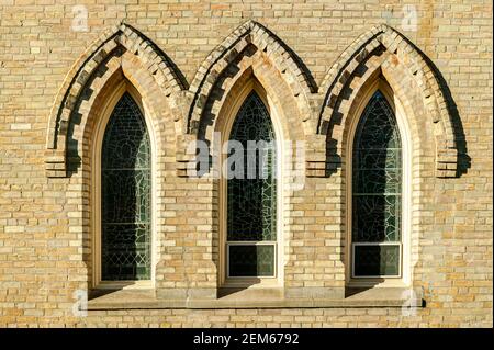 Un ensemble de fenêtres en verre au plomb encadrées de briques sur une église en Ontario. Banque D'Images