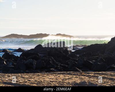 La lumière du soleil brille à travers les vagues et les embruns marins alors qu'ils s'écrasent sur les rochers près de la côte australienne Banque D'Images
