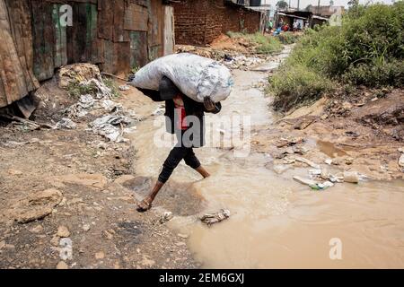 Nairobi, Kenya. 23 février 2021. Un homme transportant un sac lourd de charbon traverse une rivière d'égout locale dans les bidonvilles de Kibera. Crédit : SOPA Images Limited/Alamy Live News Banque D'Images