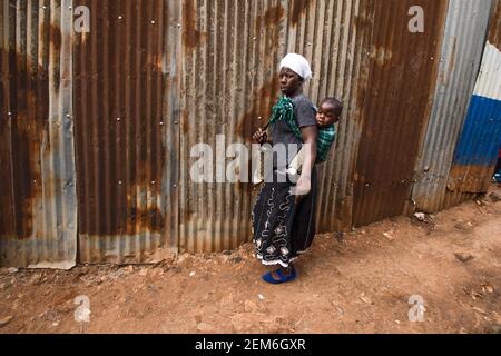 Nairobi, Kenya. 23 février 2021. Une femme marche le long d'une vieille rue dans les bidonvilles de Kibera, son petit bébé étant andainé sur le dos. Crédit : SOPA Images Limited/Alamy Live News Banque D'Images