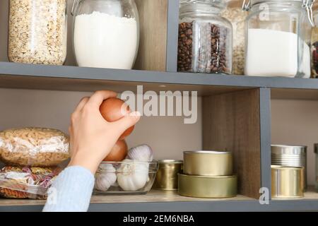 Femme prenant l'oignon de l'étagère avec des produits dans la cuisine Banque D'Images