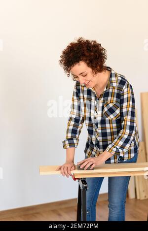 Fille faisant des tâches de bricolage et d'artisanat, vêtue d'une chemise à carreaux et d'un Jean. Elle est caucasienne et a des cheveux bouclés. Elle pond du bois sur un établi Banque D'Images