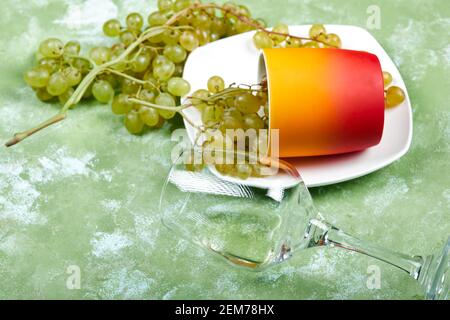 Un bouquet de raisins blancs, une tasse, un verre de vin vide sur fond vert Banque D'Images