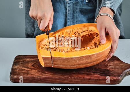 Une femme coupe à la main une tranche de citrouille avec un couteau sur la planche de bois Banque D'Images