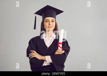 Femme diplômée de l'université dans le bonet traditionnel et le manteau debout avec diplôme en main Banque D'Images