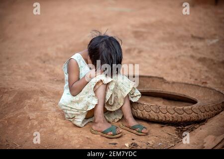 Fille asiatique UNE robe déchiquetée assise sur le sol dans un village rural. Se faubourer et pleurer, l'enfant étant taquiné et intimidé. Avoir une expression triste et triste Banque D'Images