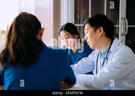 Groupe de jeunes asiatiques, hommes et femmes, médecin et infirmière s'asseoir pendant la pause dans la cantine et discuter de cas sérieux de patient à l'hôpital Banque D'Images