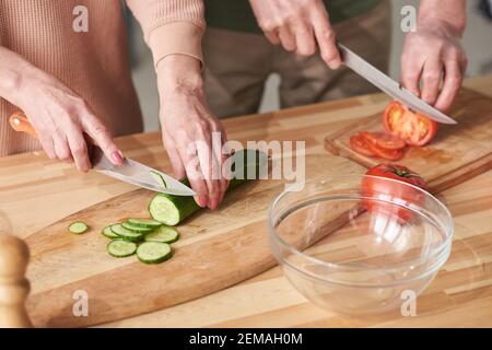 Gros plan du couple coupant du concombre frais et de la tomate sur la découpe accompagnements pour salade Banque D'Images