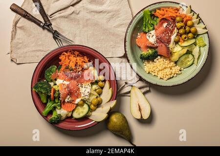 Deux bols de poke avec du saumon, du brocoli, des carottes, des poires et des pâtes ptitim. Fruits de mer et légumes. Une alimentation saine. Vue de dessus Banque D'Images