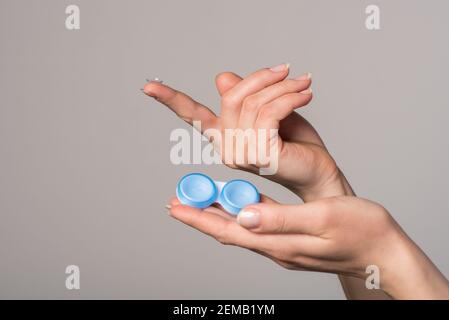 Lentille de contact souple et récipient bleu dans de belles mains femelles sur fond gris Banque D'Images