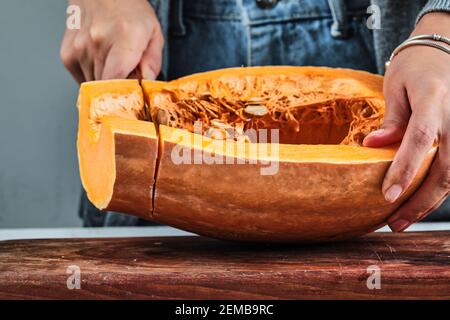 Une femme coupe à la main une tranche de citrouille avec un couteau sur la planche de bois Banque D'Images