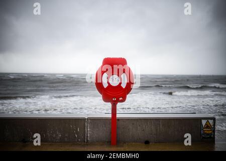 Rouge vif moderne bouée de sauvetage avertissement sur la côte de l'océan ciel de tempête. Équipement de sauvetage preserver poste d'urgence pour aider à prévenir la noyade en mer Banque D'Images