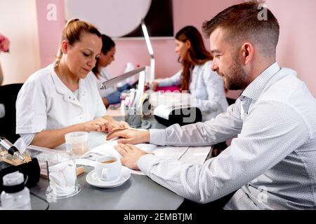 Beau type regardant ayant un traitement de manucure dans un ongle salon Banque D'Images