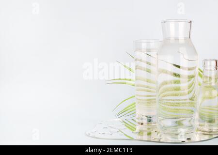 feuille de palmier déformée à travers l'eau dans le verre et les bouteilles avec miroir sur fond bleu. Décoration maison, écologique, eau pure, concept de jardinage.espace copie Banque D'Images